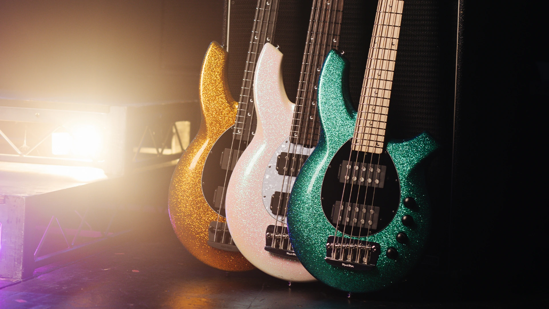 Three Music Man Bongo basses in various colours on a stage.