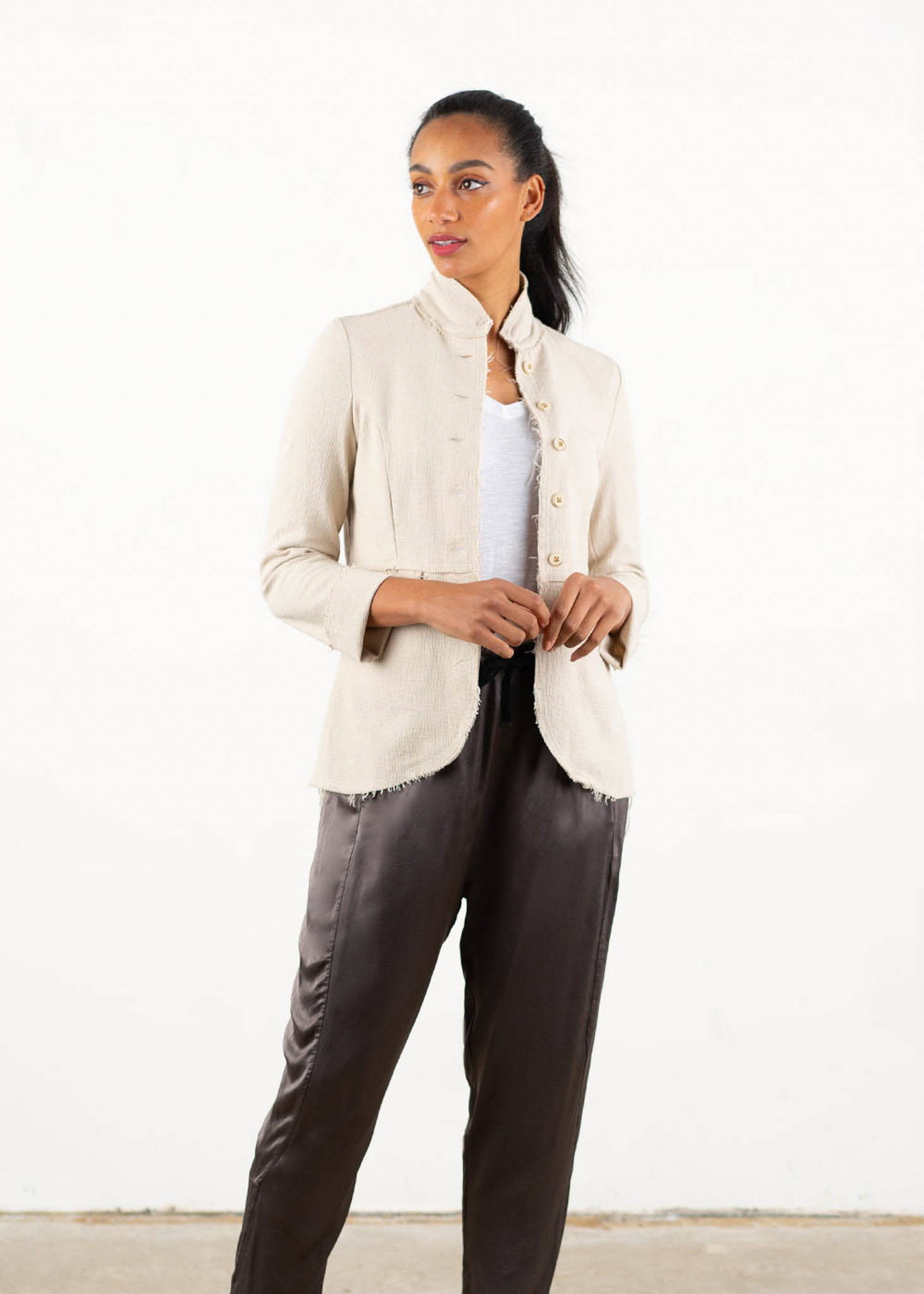 A model wearing a white cotton mix jacket with raw hem detailing over a white top and dark grey trousers