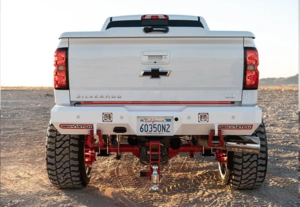 Rear straight-on view of Juan's white 2018 Chevrolet Silverado 2500HD showing lifted stance, red suspension, and horn installation underneath, photo 3