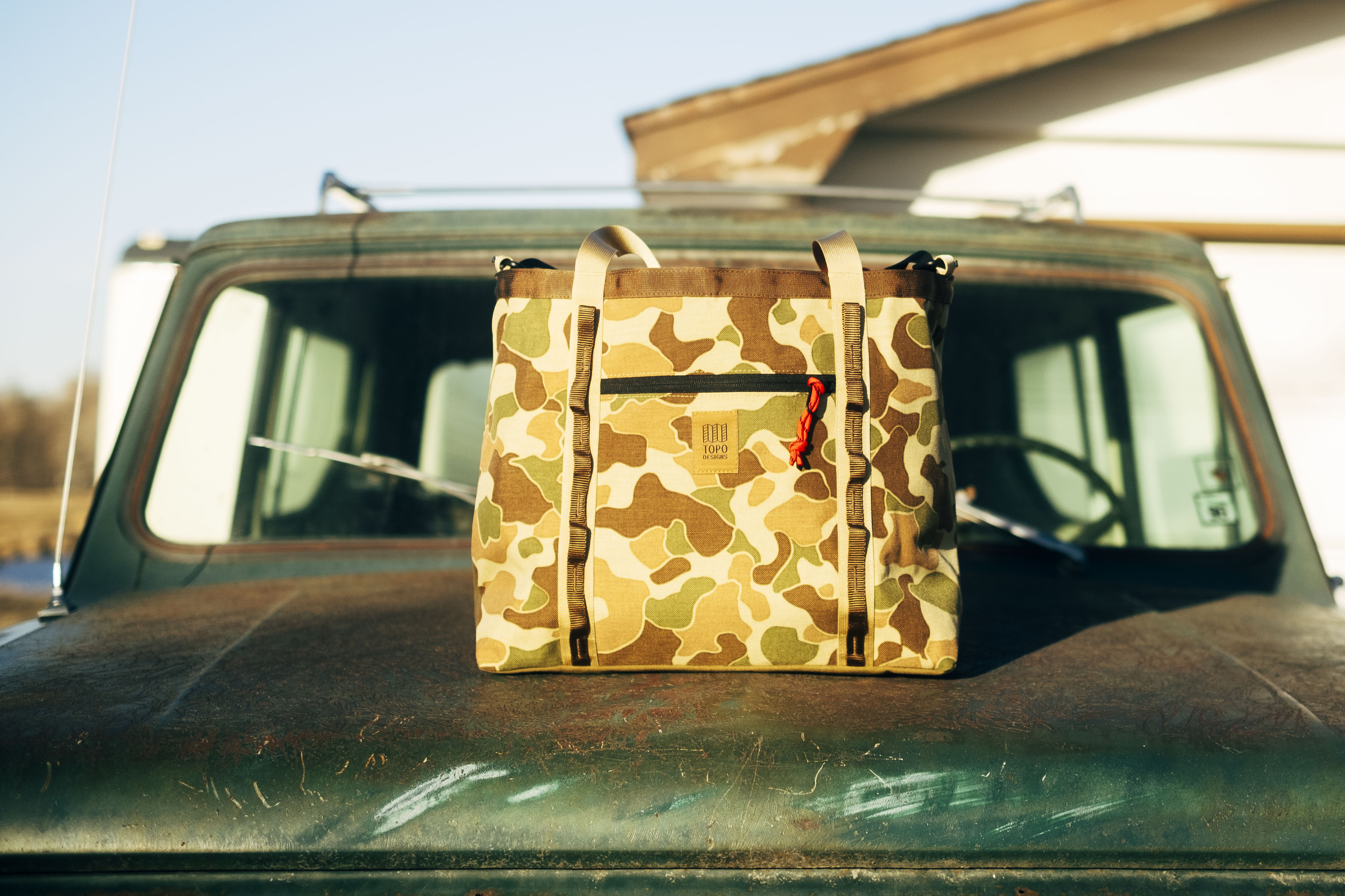 A camouflage bag resting on a vintage vehicle hood.