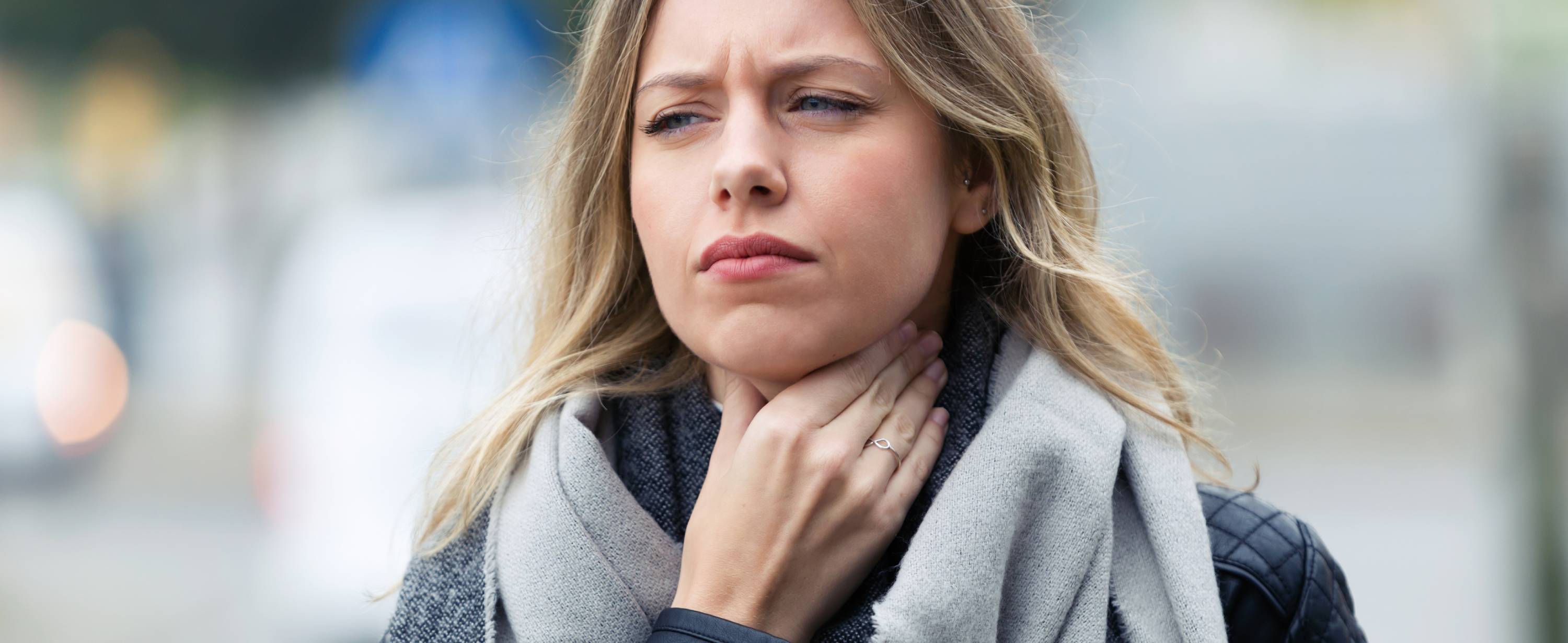 En kvinne med plaget ansiktsuttrykk holder en hånd rundt halsen – kanskje er hun plaget av slim, kløe eller irritasjon i halsen som følge av allergi?