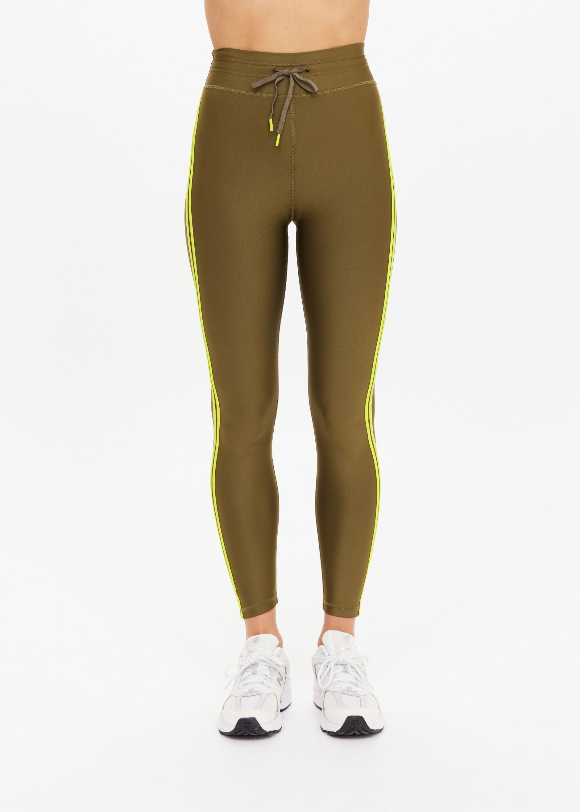 Woman wearing olive green leggings with yellow side stripes and white sneakers.