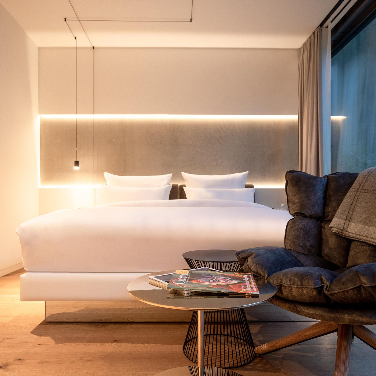 Modernes Schlafzimmer mit großem Bett, stilvollem Stuhl und warmer Beleuchtung.