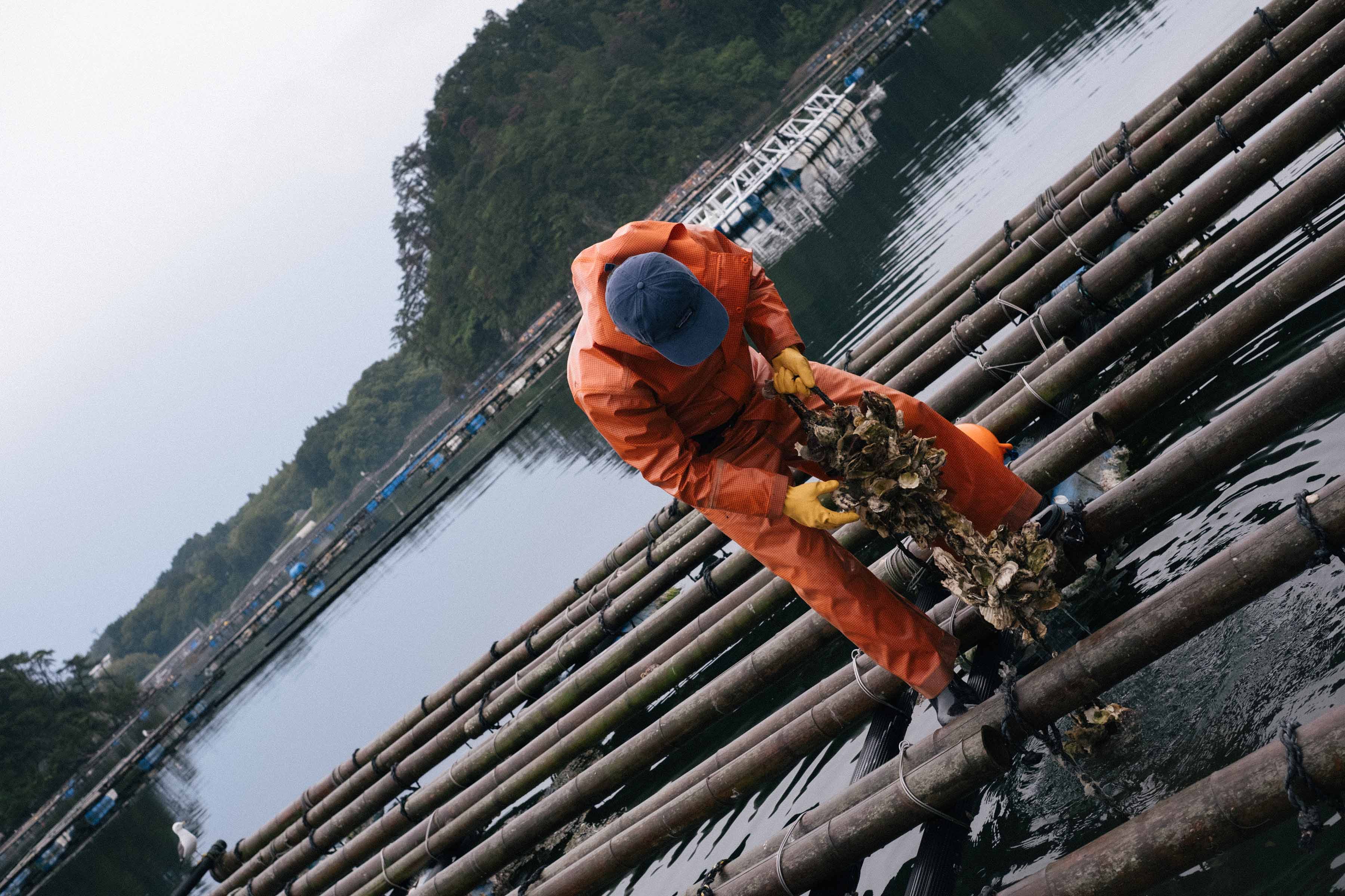 Person in an orange suit working on bamboo structures over water.