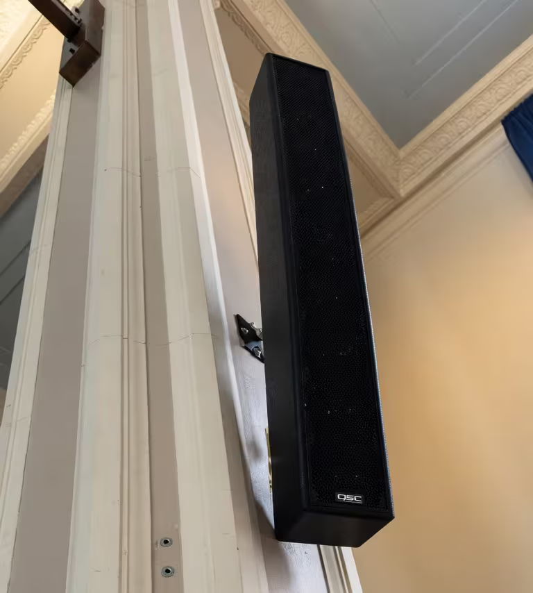 A tall black speaker mounted on a wall.