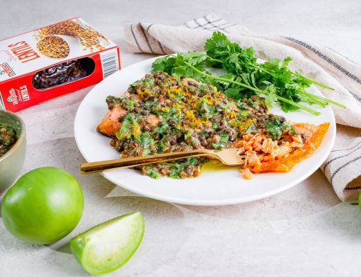 A plate of salmon with greens, lime, and a box of pasta.