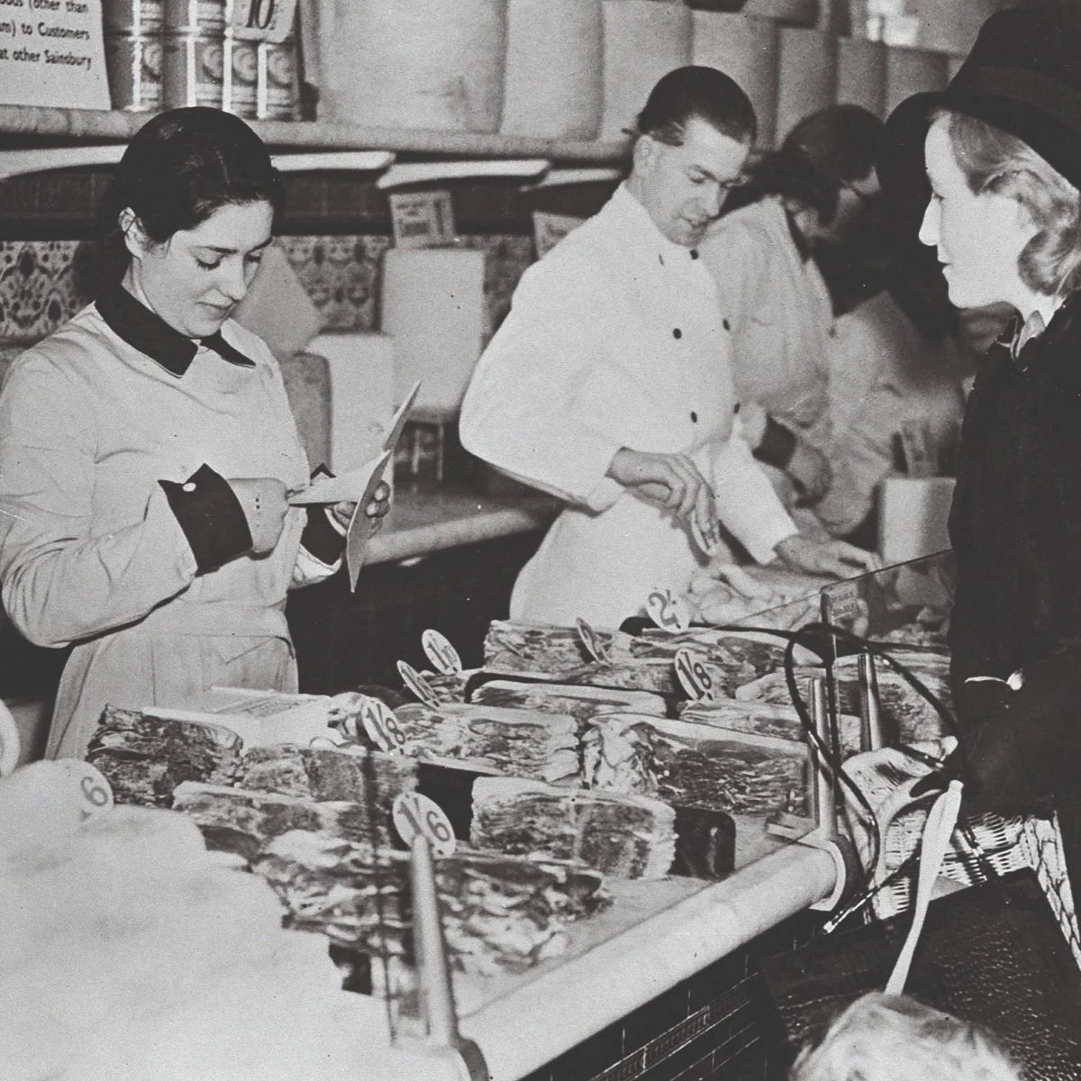People shopping at a butcher shop, examining meat and goods.