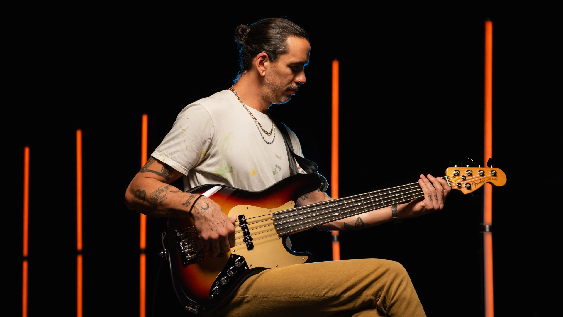 A musician playing a Fender American Ultra II 5-string Jazz Bass guitar on stage with glowing vertical lights.