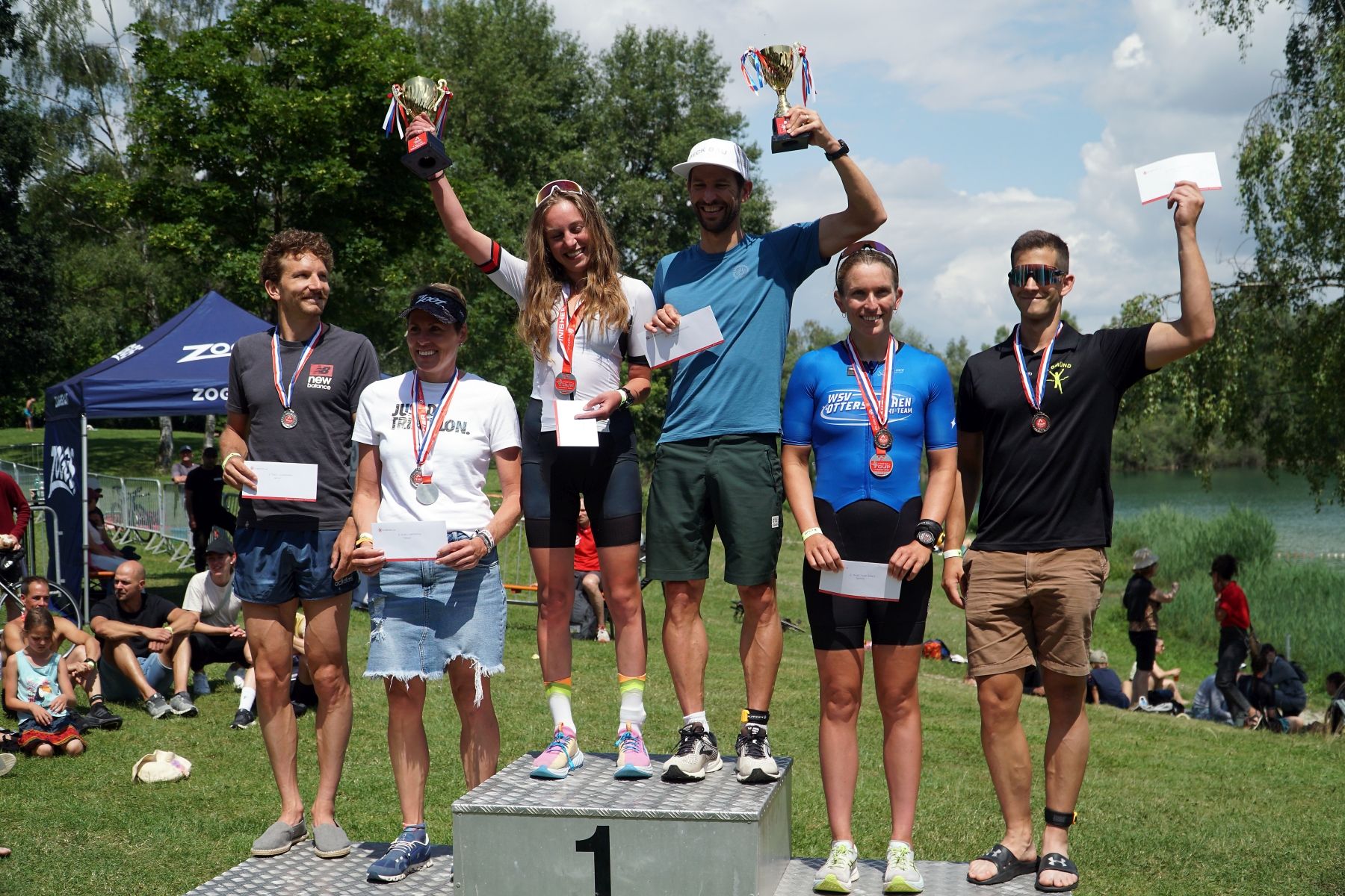Die Podest-Platzierten stehen auf dem Siegertreppchen des triathlon.de Cup Landshut 2025, halten ihren Gewinn in den Händen und lächeln in die Kamera.