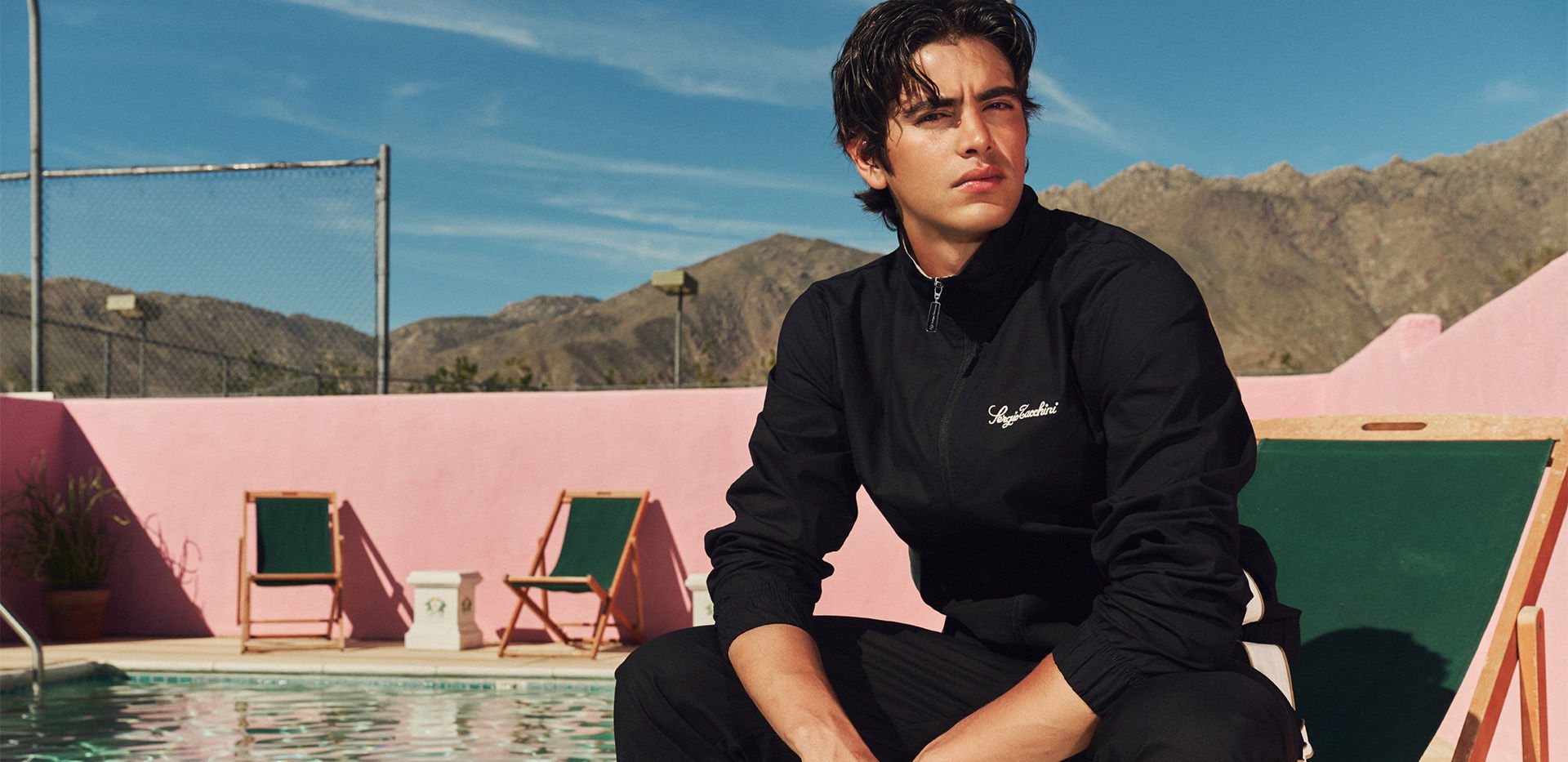 Young man sitting by a pool with mountains in the background.