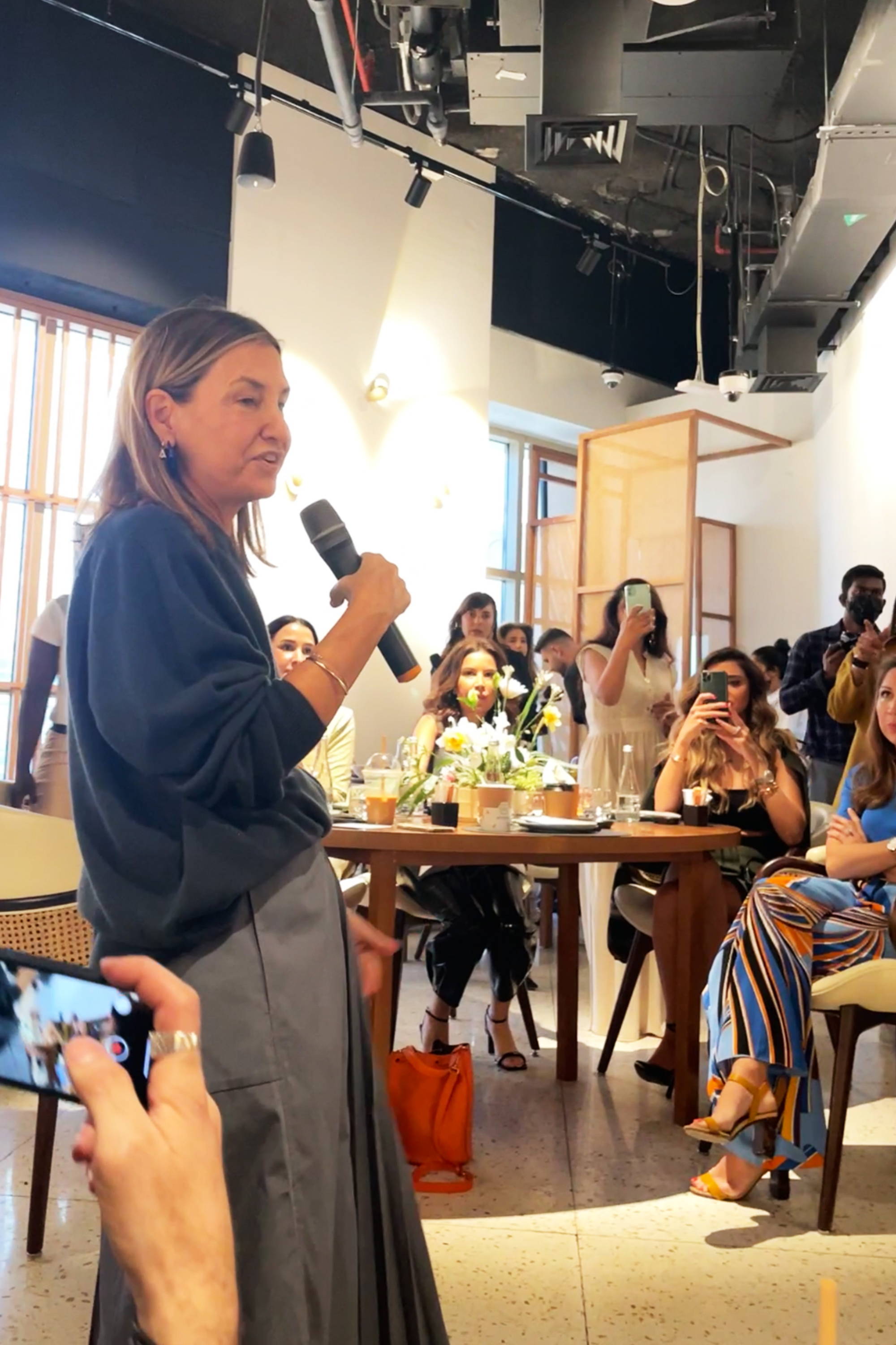 Woman speaking at an event, audience engaged, casual setting.