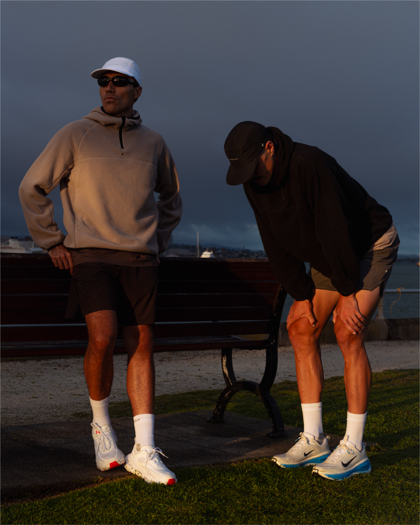 Two men in athletic wear standing near a bench at dusk.