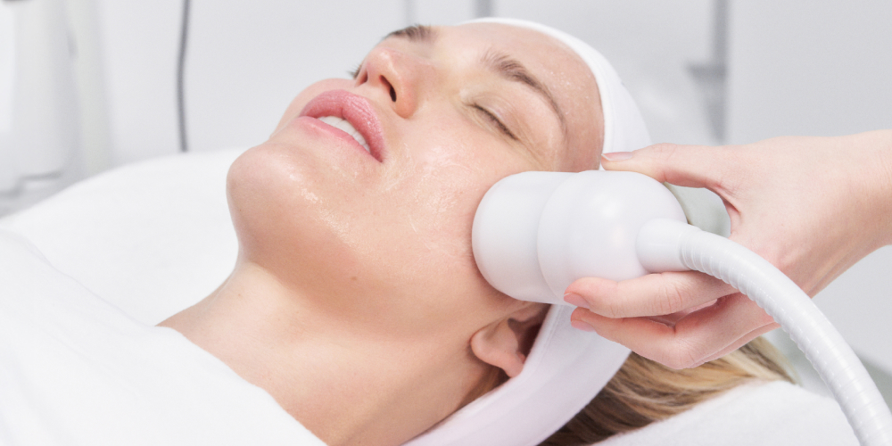 Woman receiving a facial treatment with a handheld device in a spa setting.