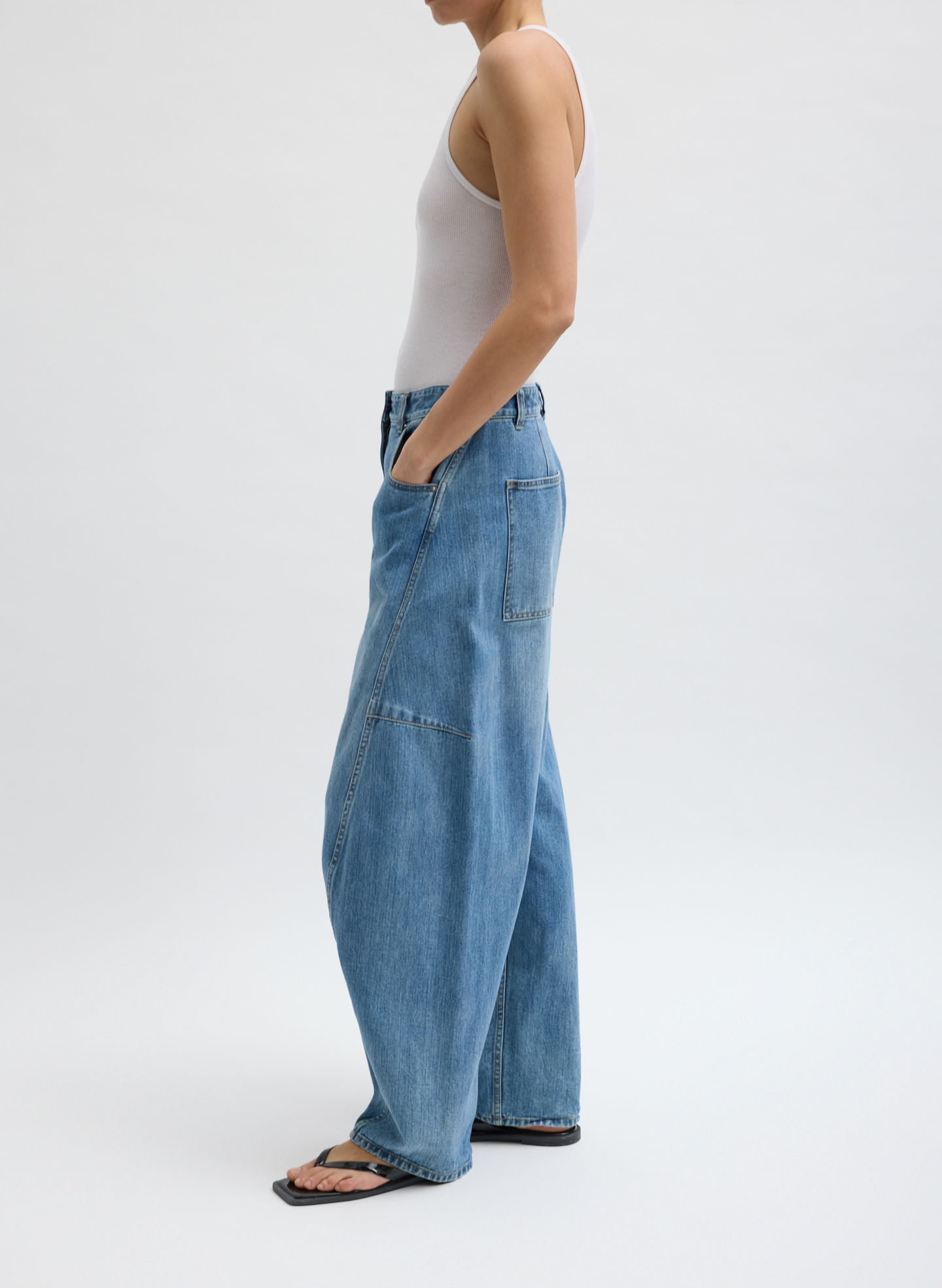 A person wearing a tank top and baggy jeans, standing sideways.