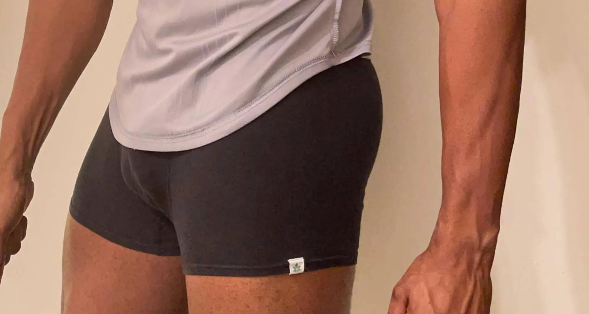 man wearing a light gray shirt with black trunks underwear flexing his arms