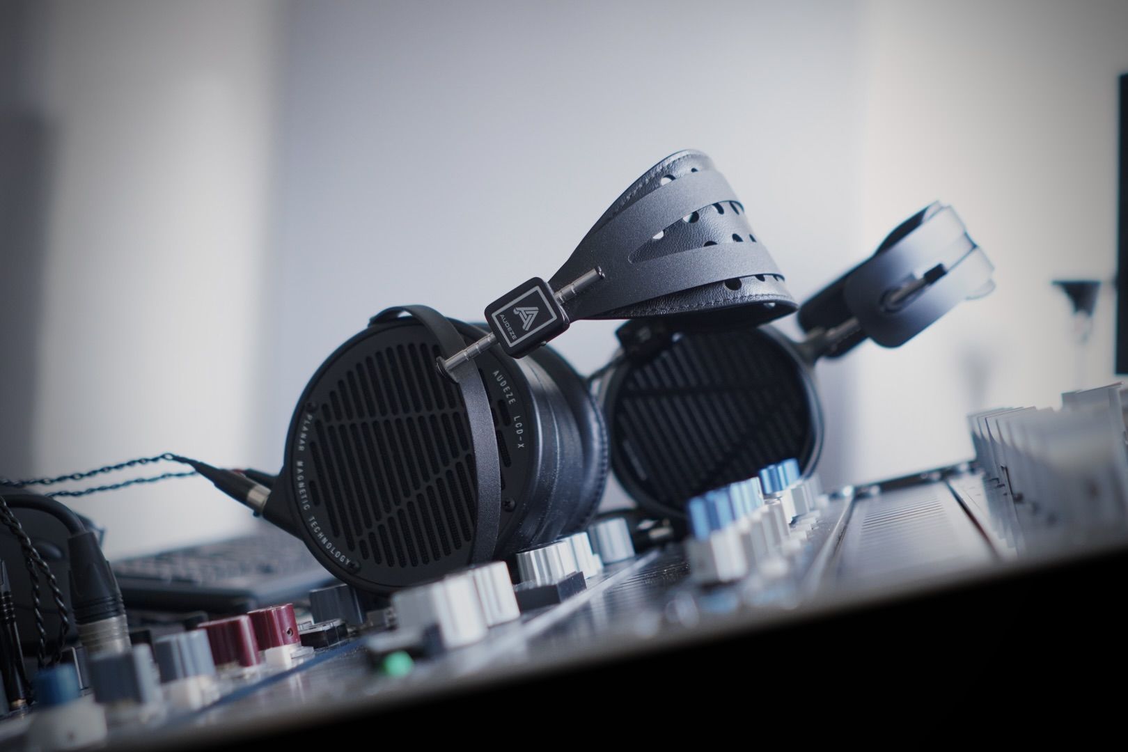 Audeze LCD-X headphones resting on a mixing console with various dials and knobs.