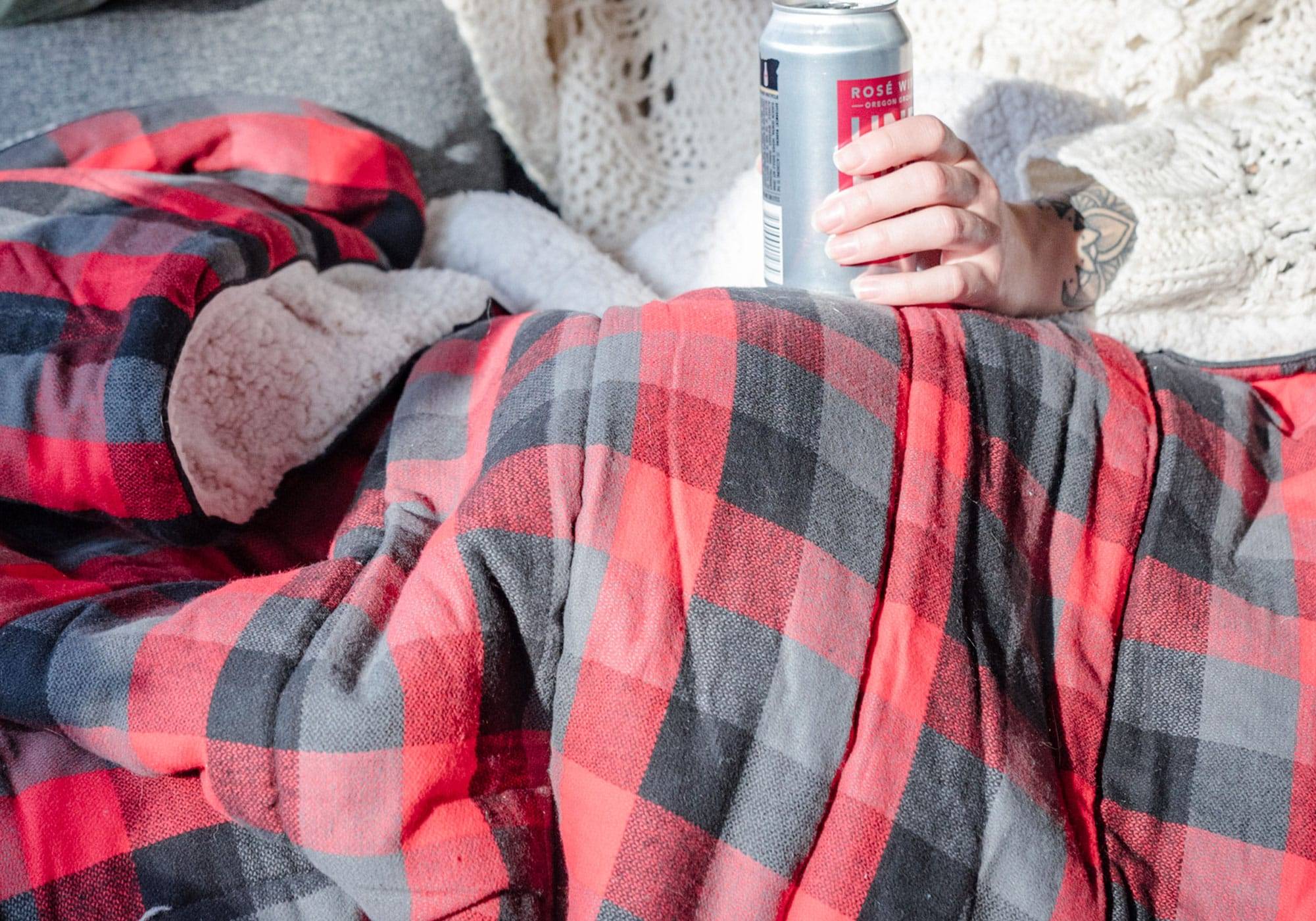Woman holding canned wine under a flannel sherpa blanket