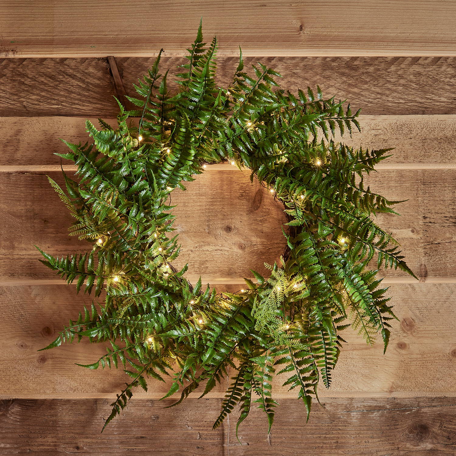 An artifical fern wreath with micro lights against a wooden backdrop.