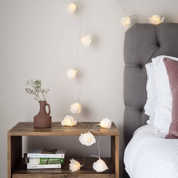 A bed with rose fairy lights draping from the ceiling on to the side table.