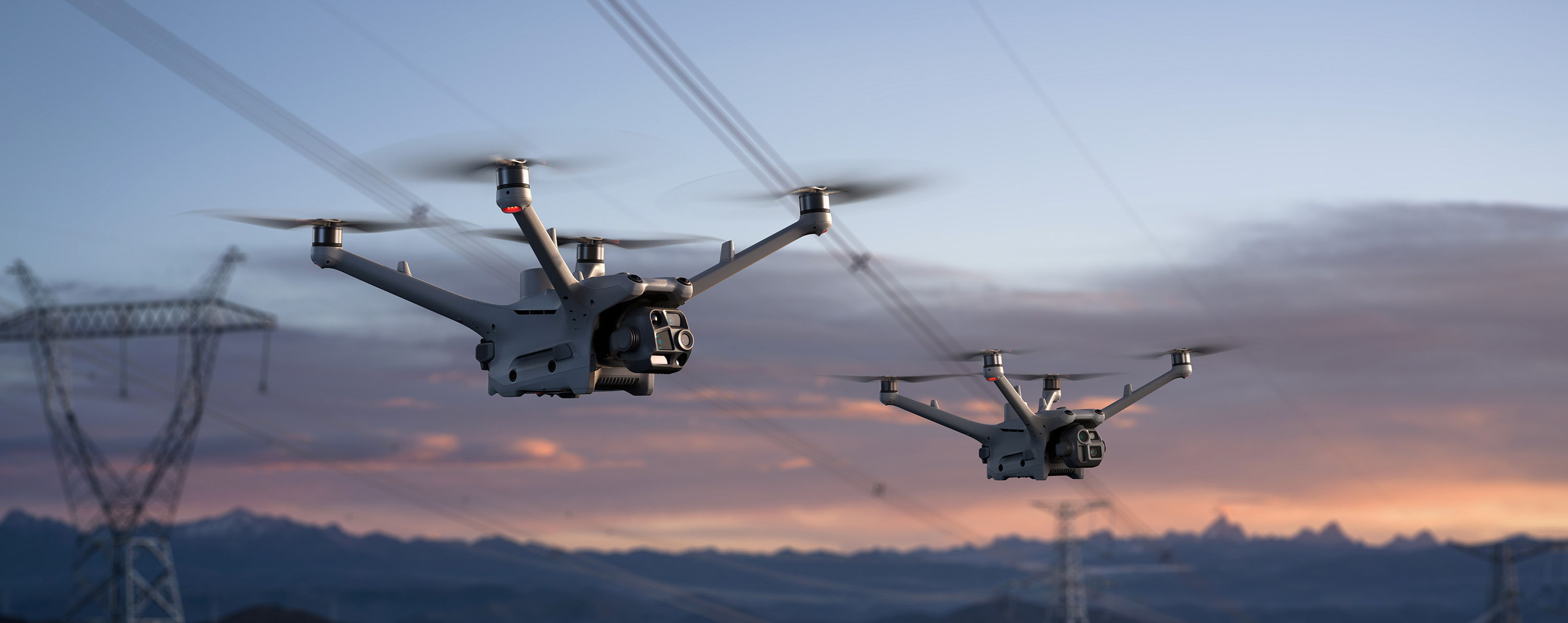 Two DJI Matrice 4D series drones flying near power lines during sunset.