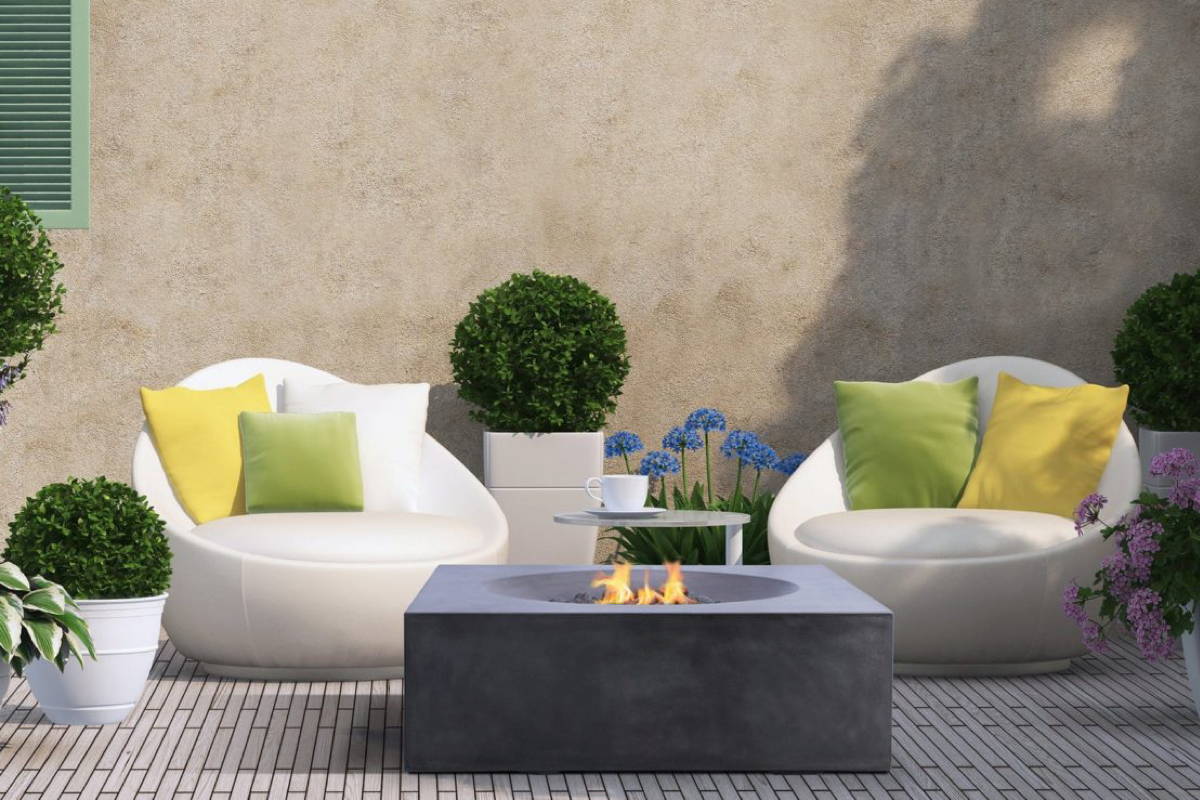 A cozy patio with white chairs surrounding a blazing modern lightweight concrete fire pit.
