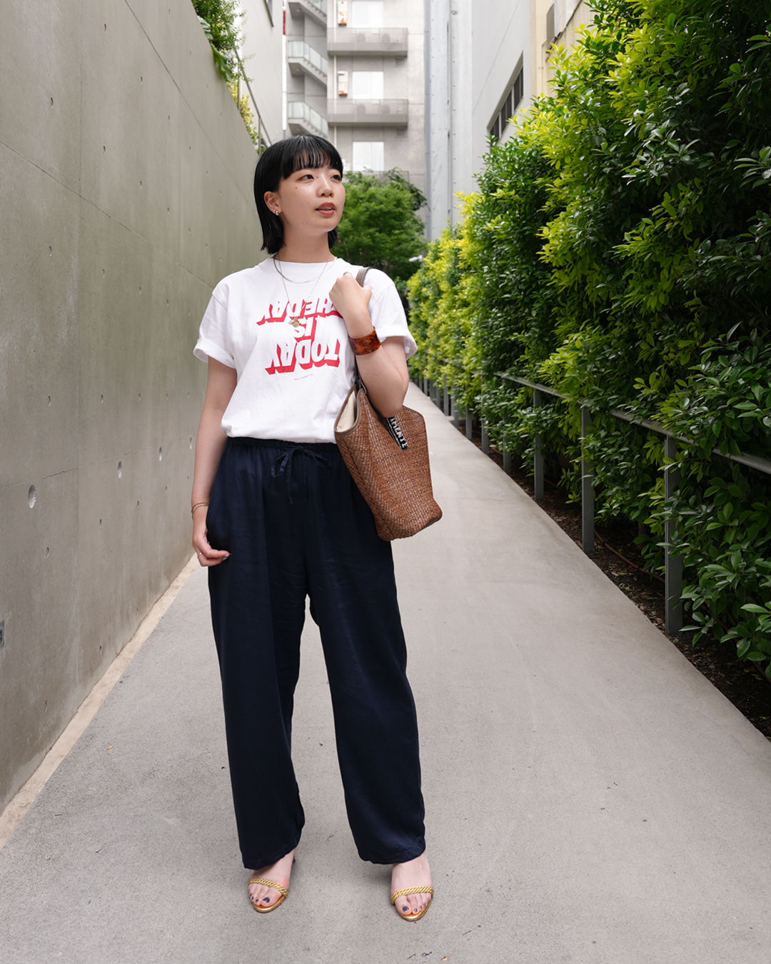 Woman in casual outfit standing on a pathway surrounded by greenery.