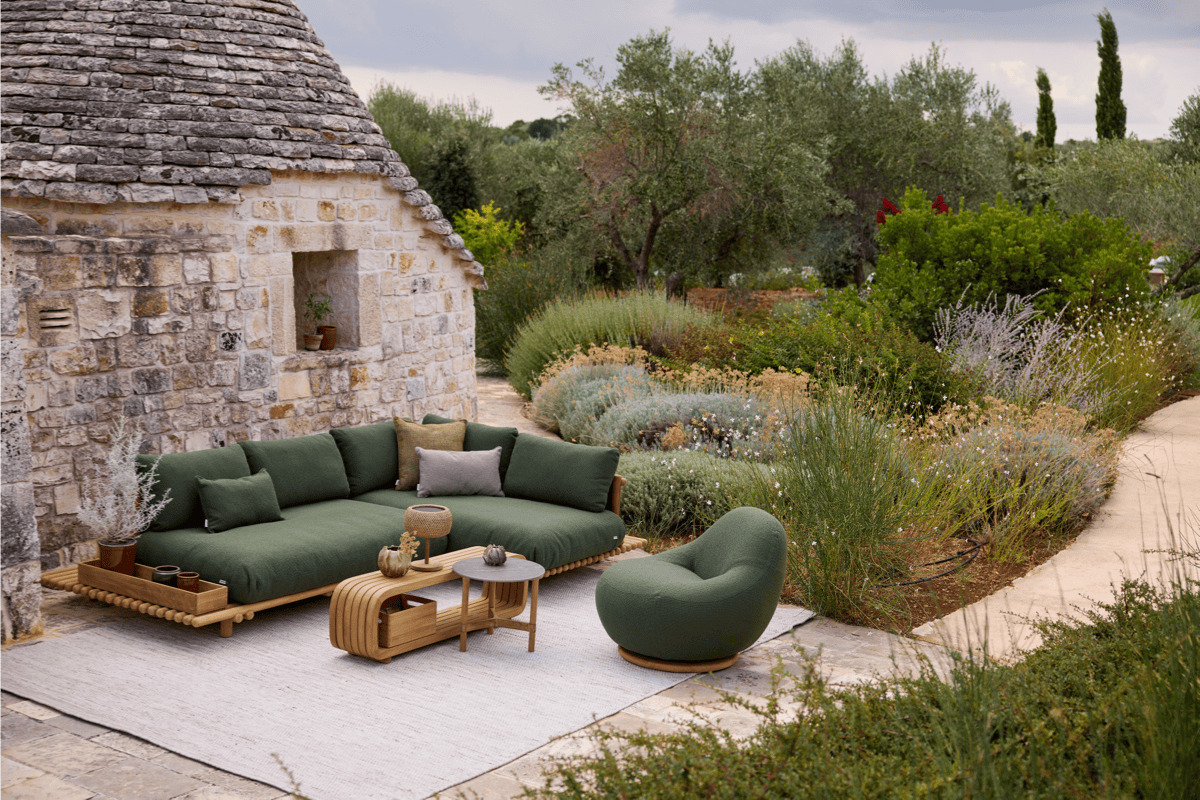 Low-maintenance garden lounge with deep green outdoor sectional, weather-resistant seating, stone walls, and drought-tolerant planting