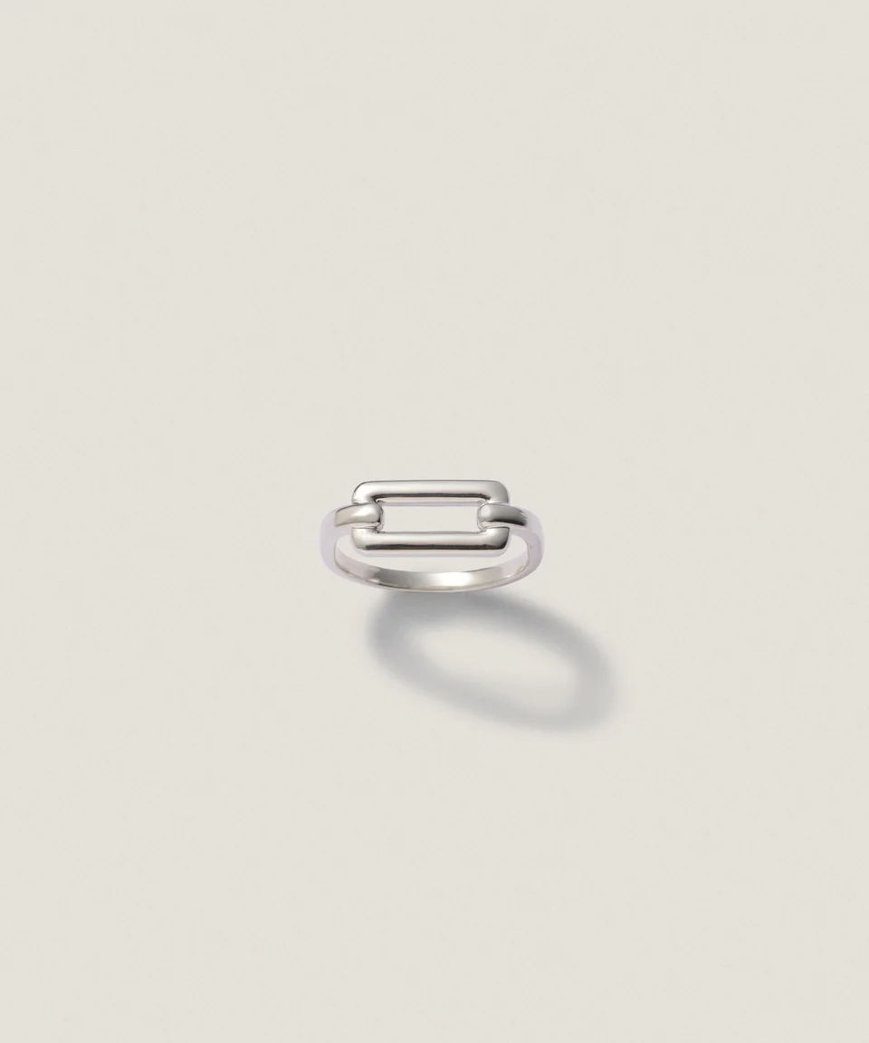 A simple silver ring with a rectangular design on a neutral background.