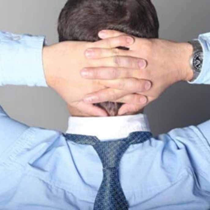 A man wearing his tie backwards with his hands on the back of his head