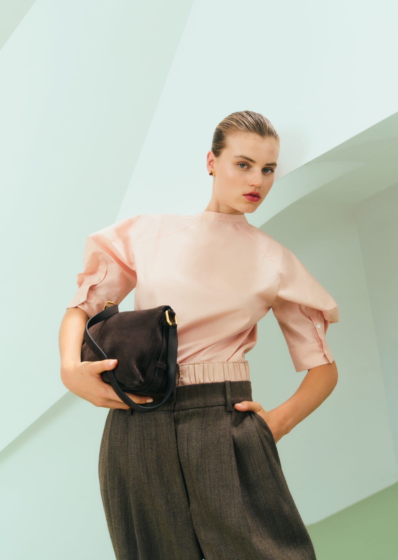 Fashion model wearing a pink top and holding a black bag.