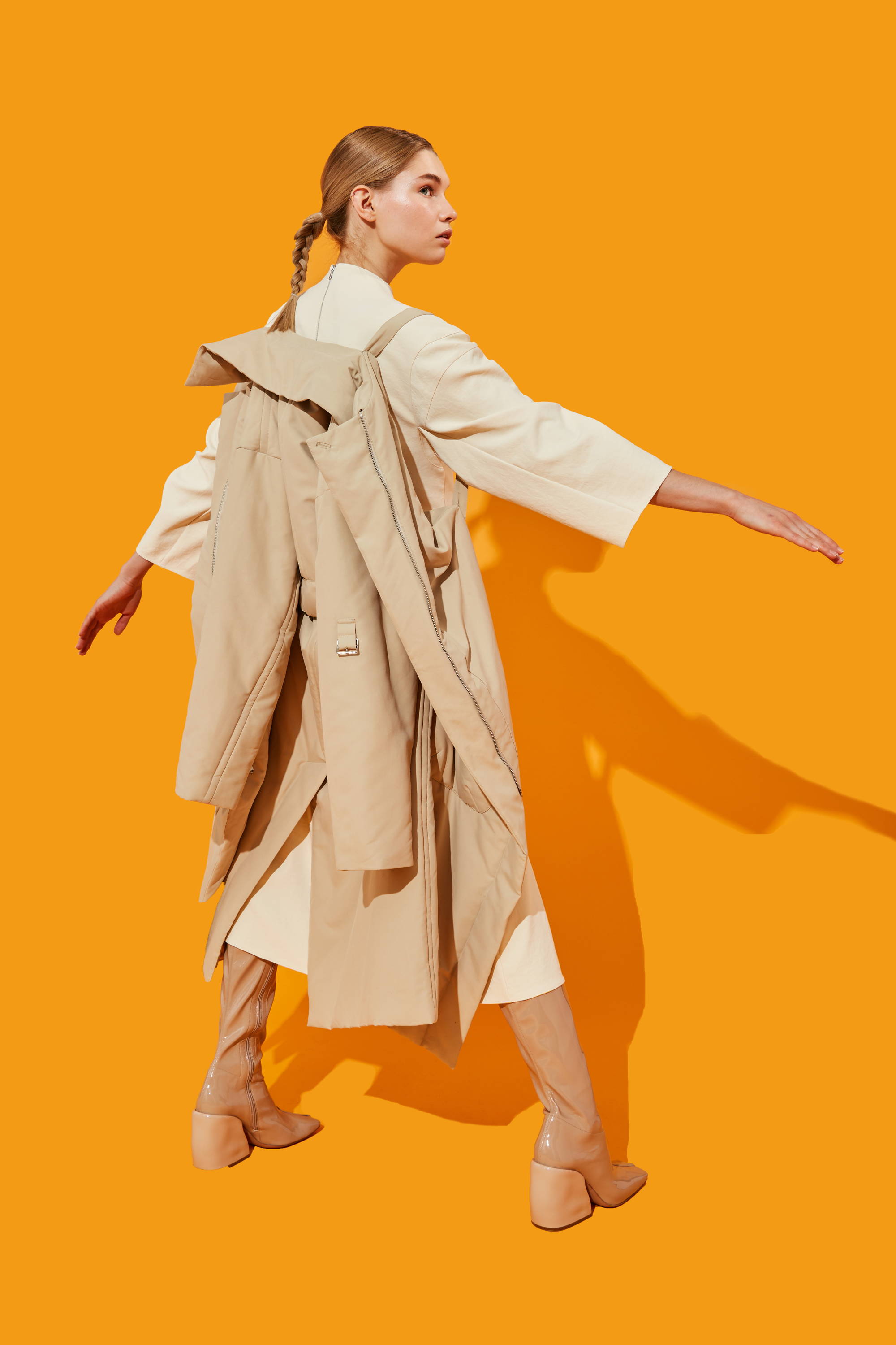 Model in a beige outfit against a bright orange background.