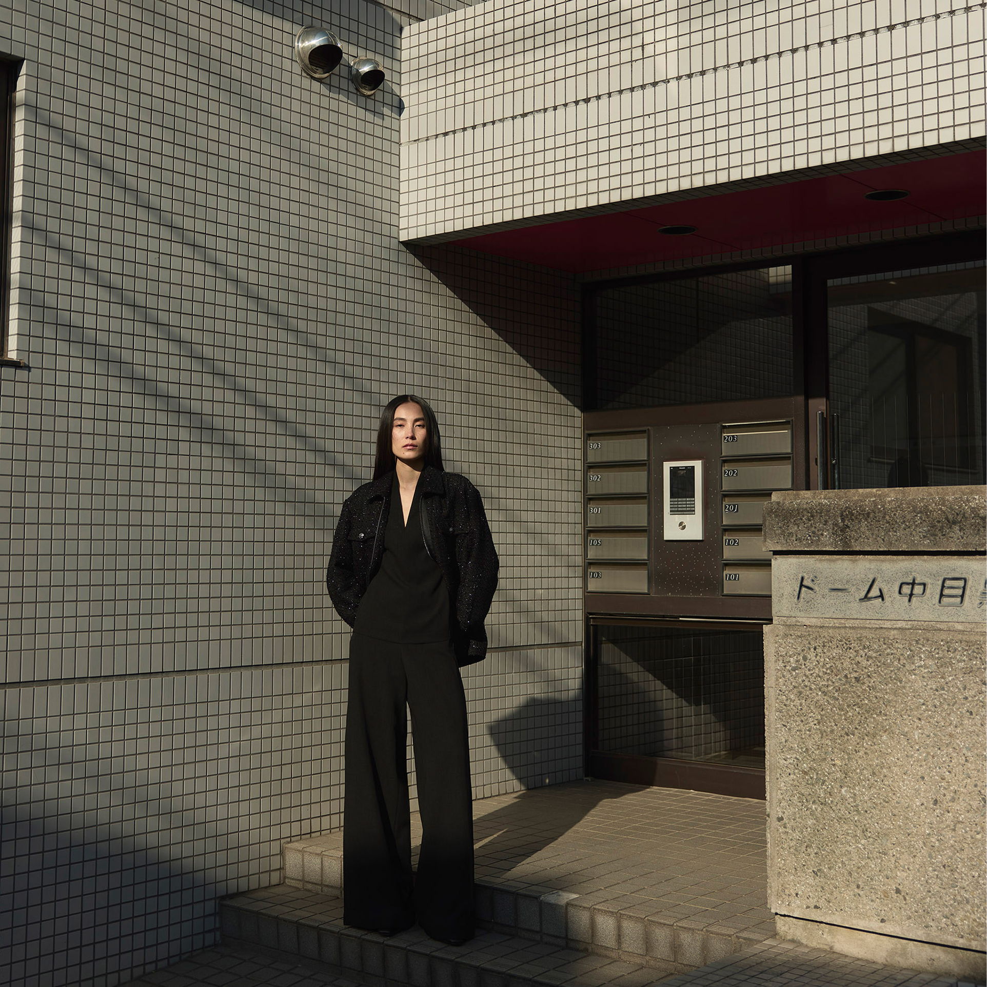 Person in black outfit standing in front of a tiled building entrance.