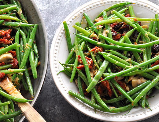 Stir-fried green beans with sun-dried tomatoes and mushrooms in bowls.