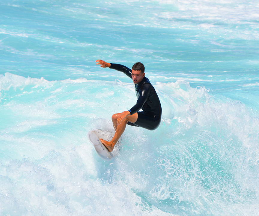 A photo of a male surfer with short hair riding his surfboard on top of a foamy small ocean wave.