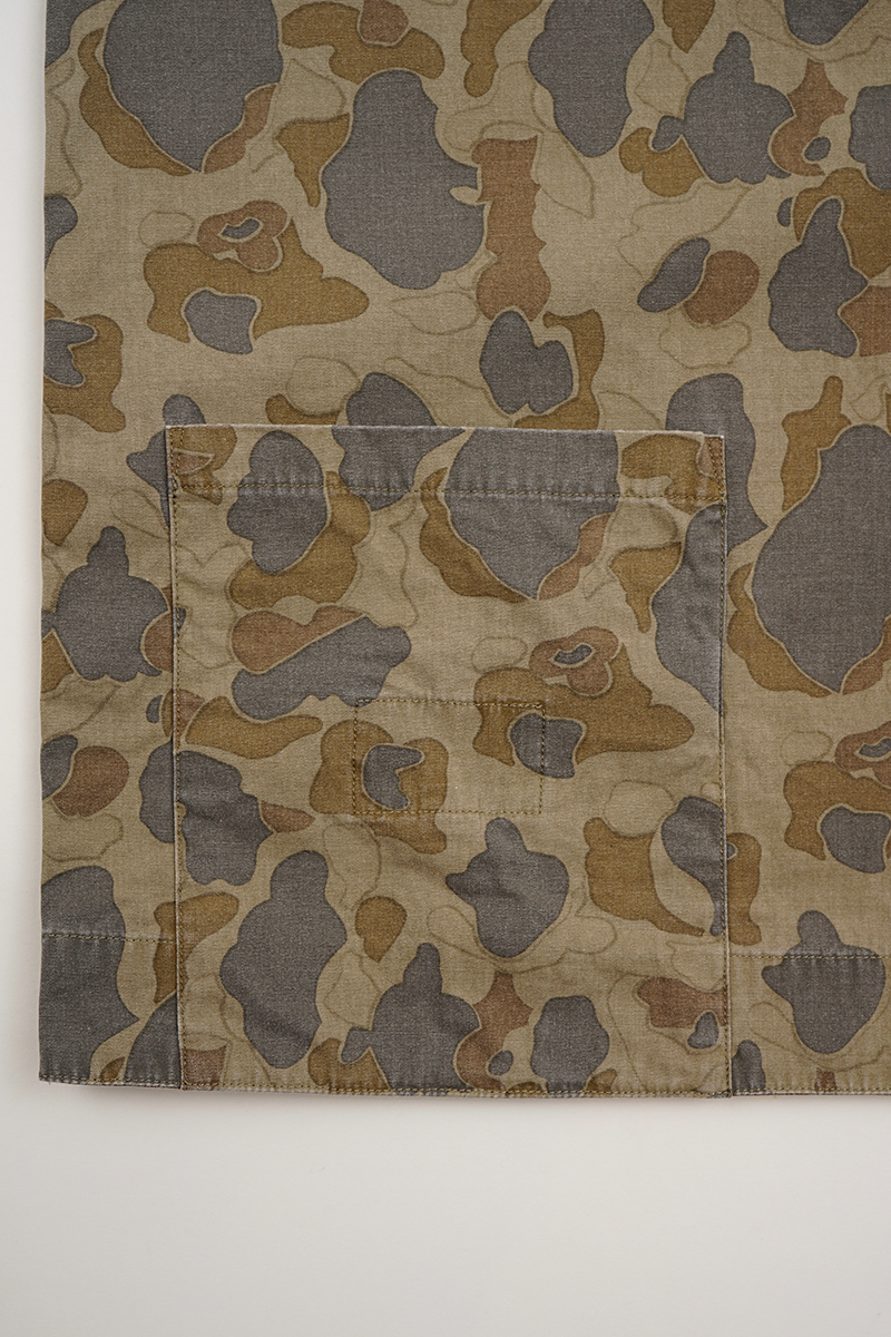 Camouflage fabric with brown and gray patterns and a pocket detail.