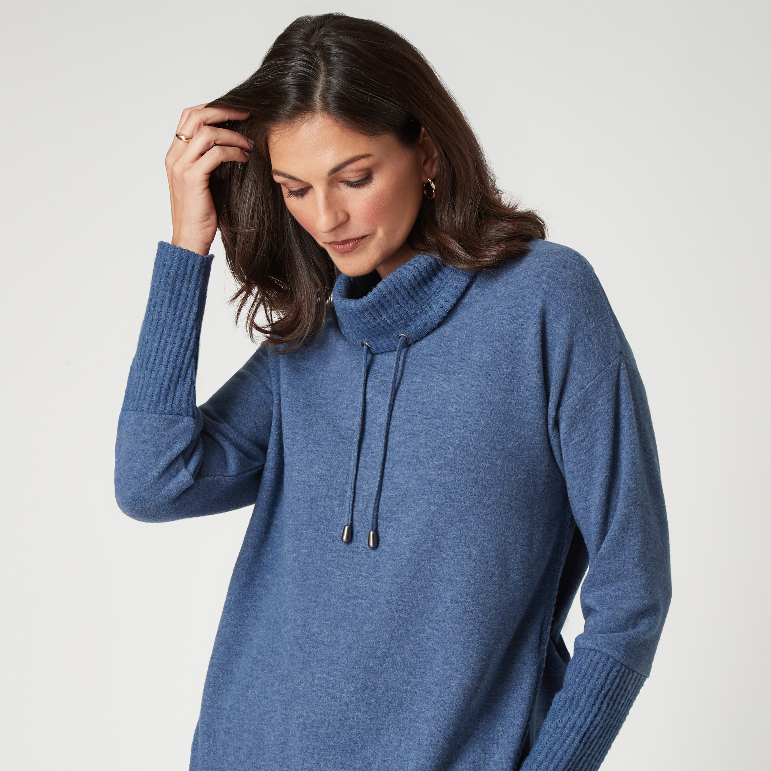 Woman wearing a blue cowl neck sweater, looking down thoughtfully.