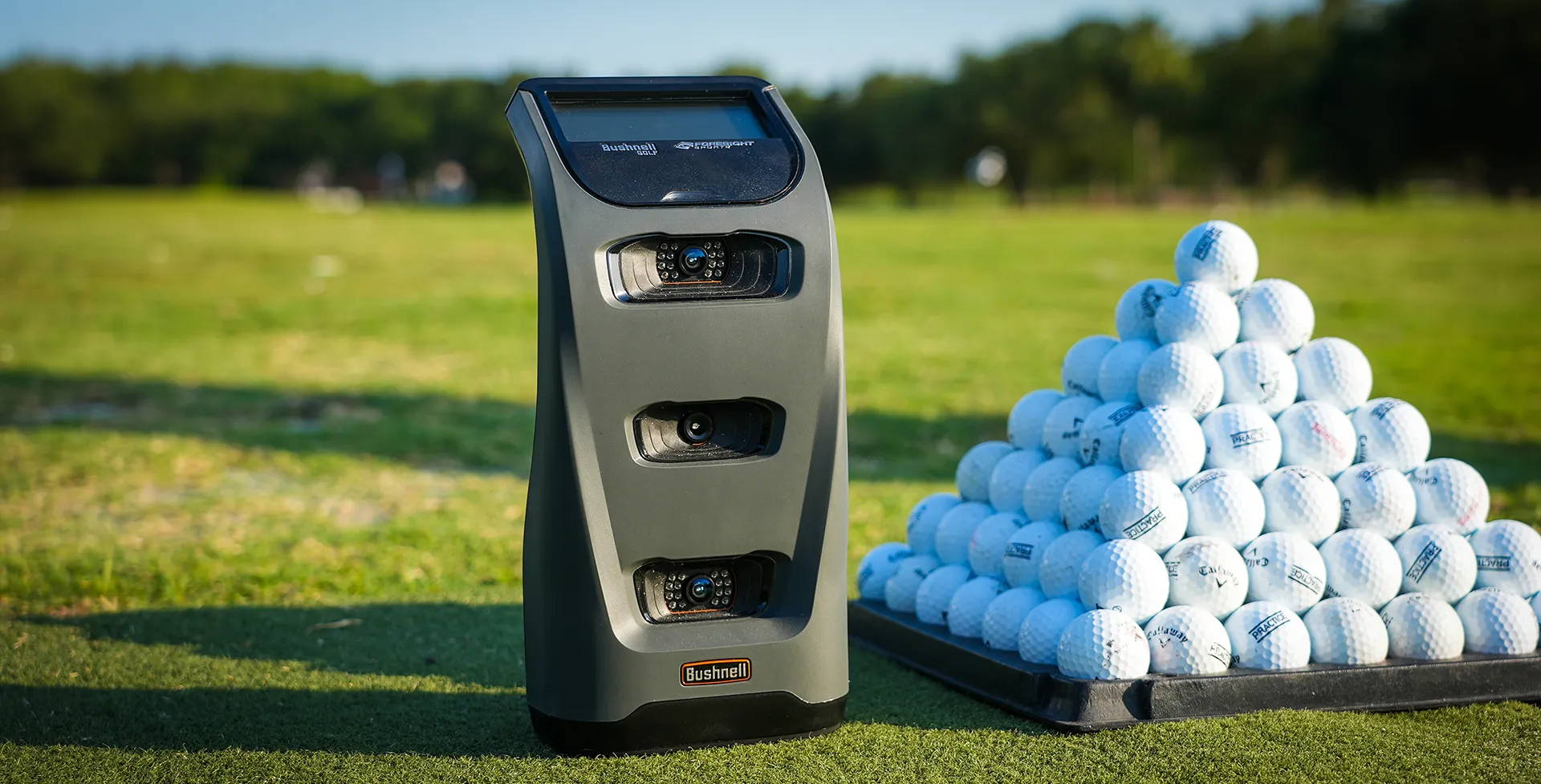 A Bushnell Launch Pro Launch Monitor with a pyramid of golf balls at the range