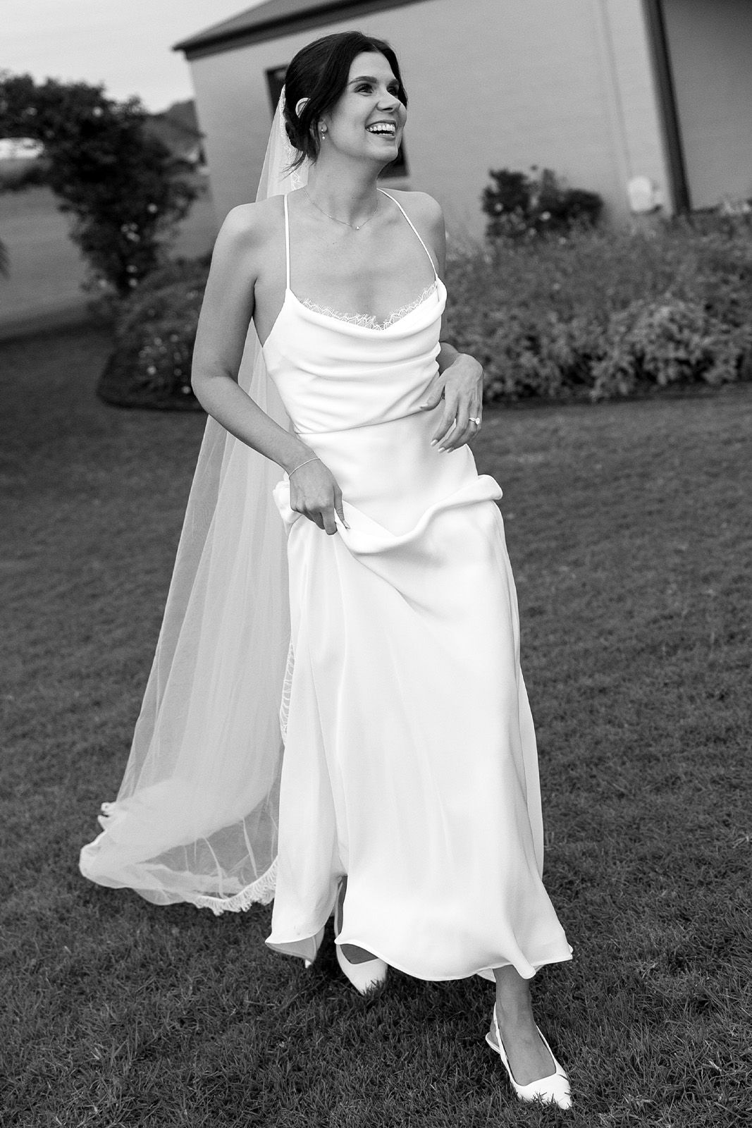 Bride in a flowing white dress and veil, smiling in a garden setting.
