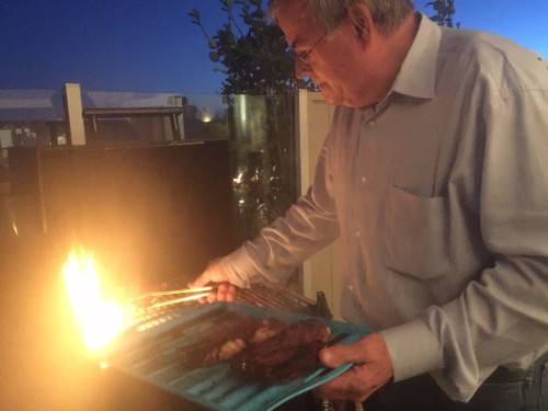 Picture of Frank Fitzpatrick, with grey hair, glasses and blue and white shirt grilling steaks on a barbeque