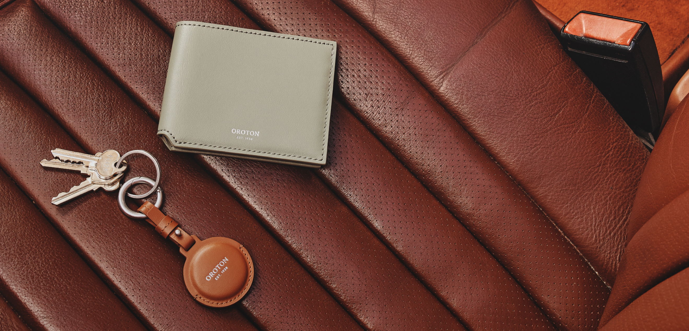 A wallet, keys, and a keychain on a brown leather surface.