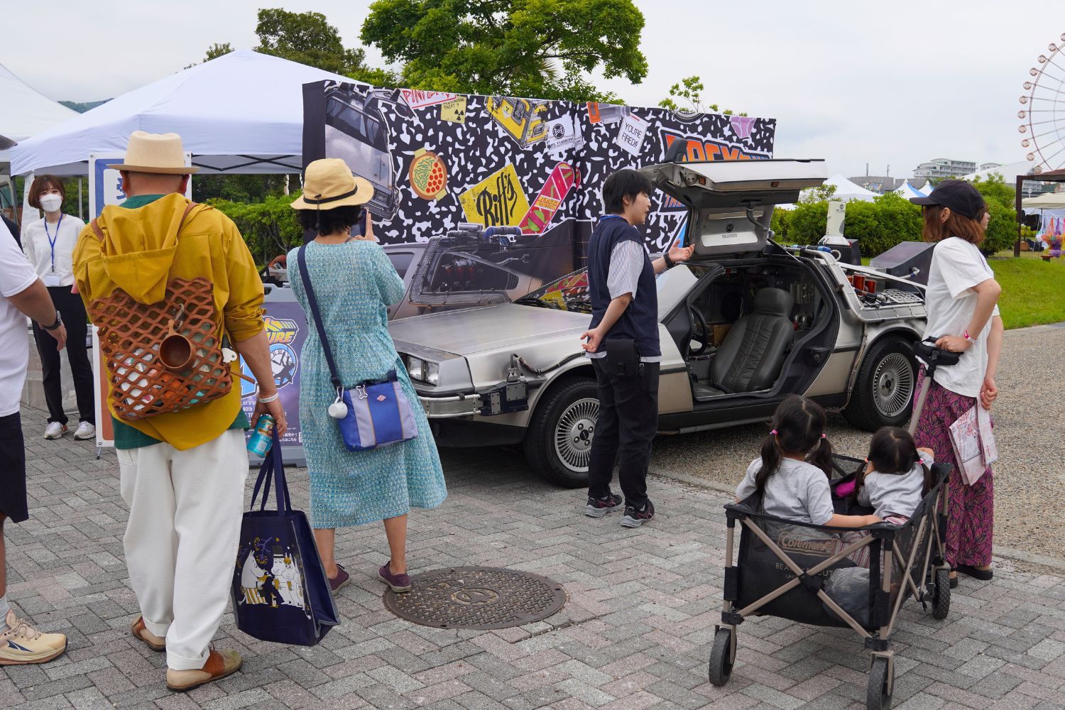 People gathered around a DeLorean car at an outdoor event.