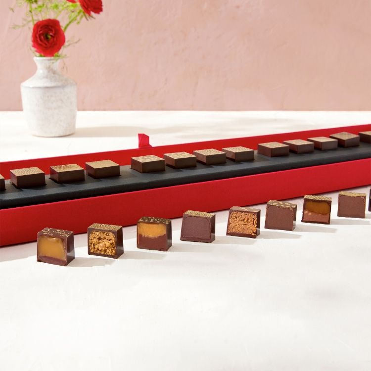 Chocolate squares displayed on a red tray with a vase of flowers.