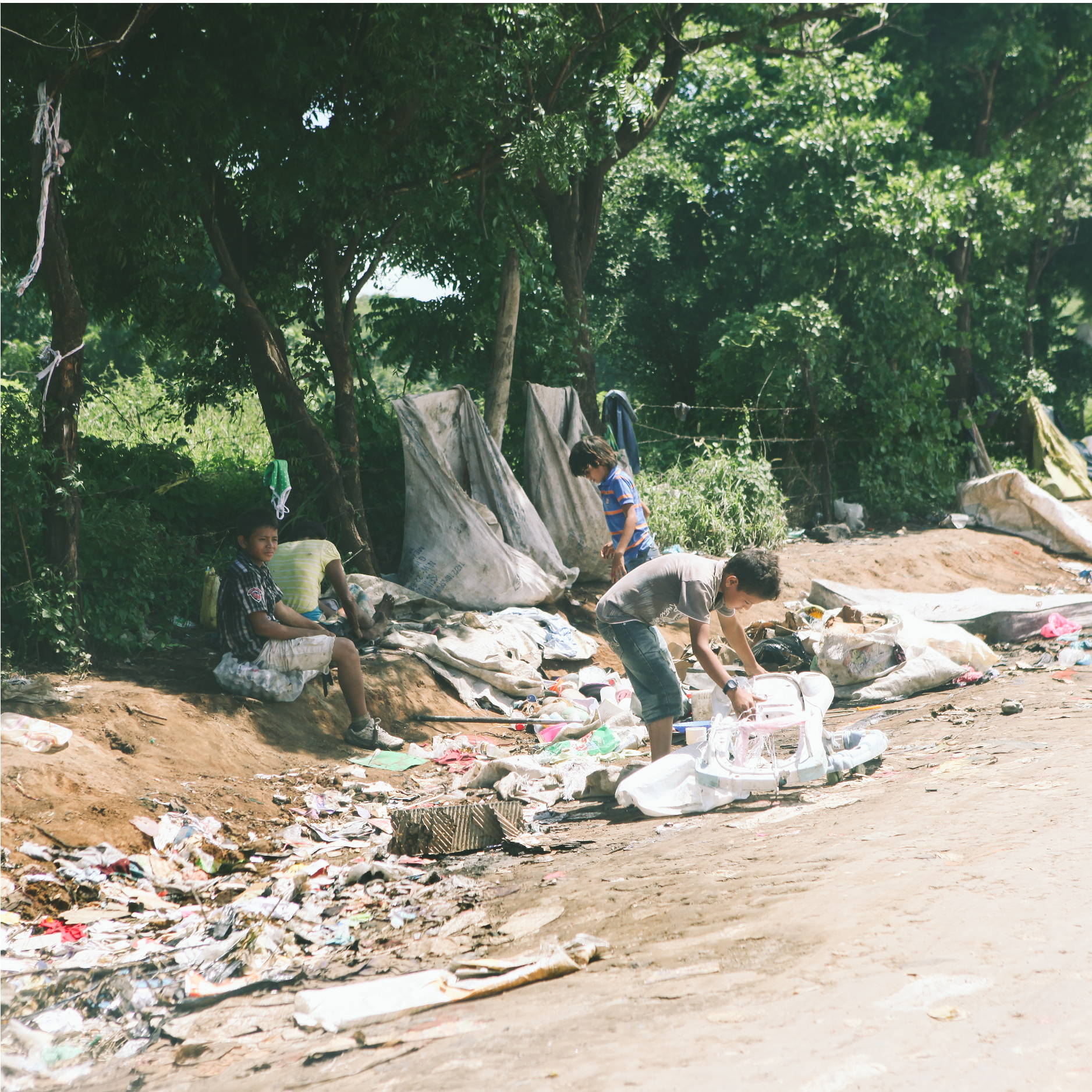 two young boys dig through trash that is strewn along the side of a nicaraguan dirt road as they look for food. 