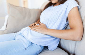 Pregnant woman sitting on a couch, holding her belly.