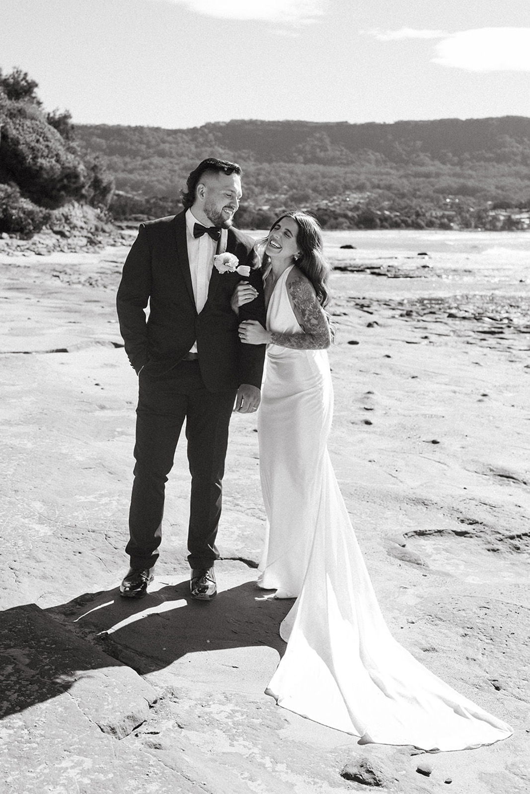 Couple in wedding attire smiling on a beach.