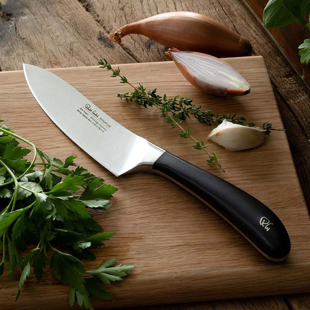 Signature Cook's Knife on a wooden cutting board with herbs and shallots.