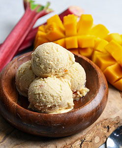 Scoops of mango rhubarb ice cream in a wooden bowl with mango and rhubarb.