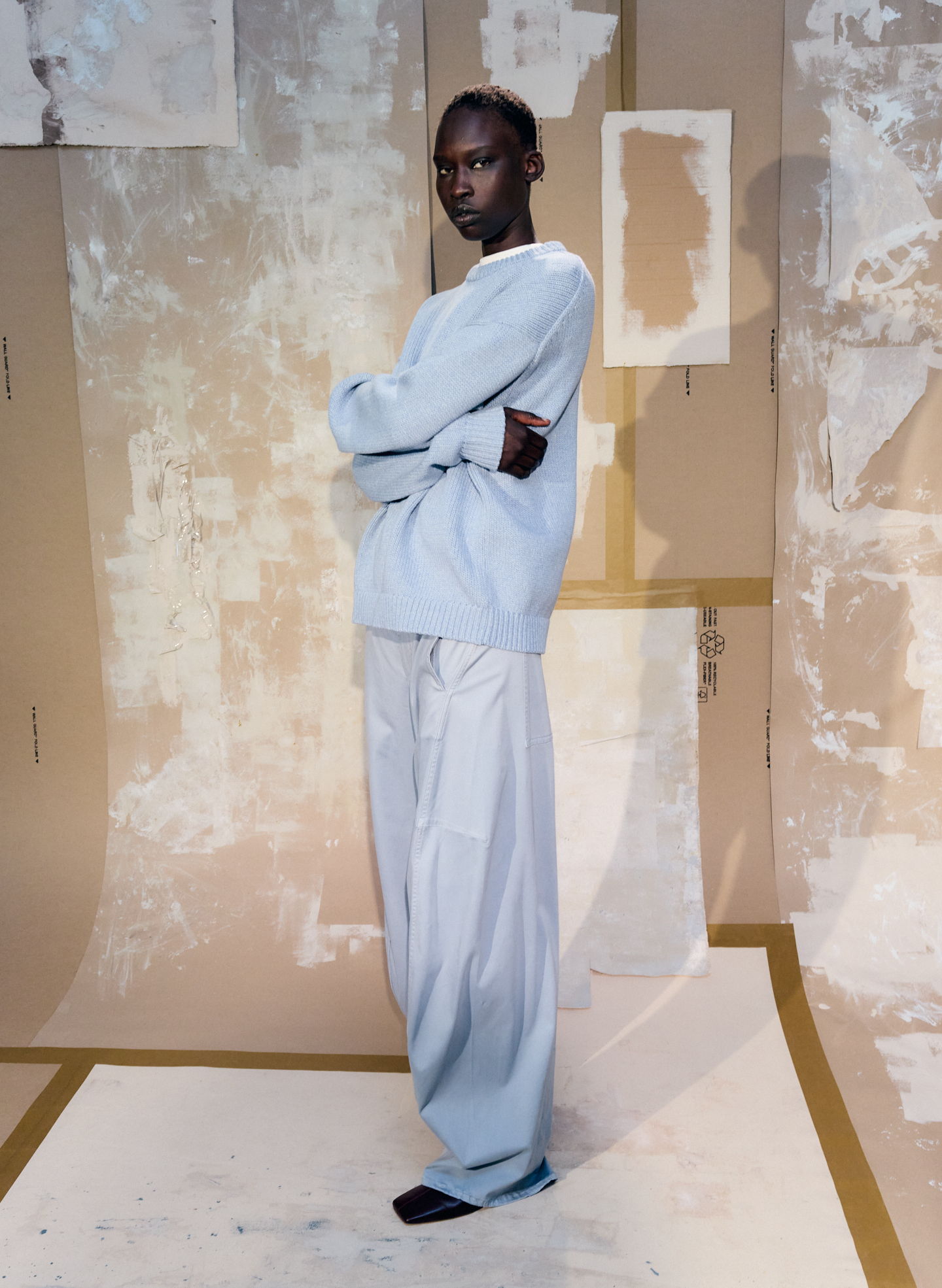 Model in oversized light blue outfit posing against a textured backdrop.
