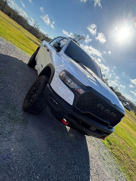 Front quarter view of white RAM pickup with off-road wheels and red tow hooks on gravel