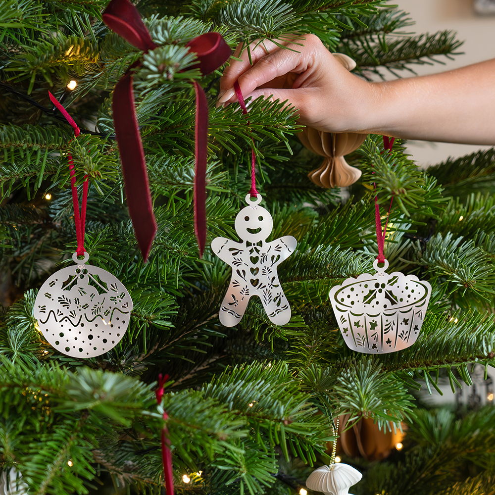 A hand hanging festive ornaments on a Christmas tree.